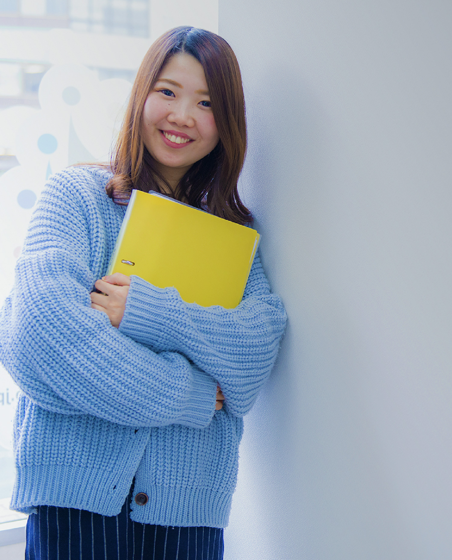 女性が黄色のノートを持って笑っている写真